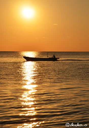 輝く光の帯を横切る漁船